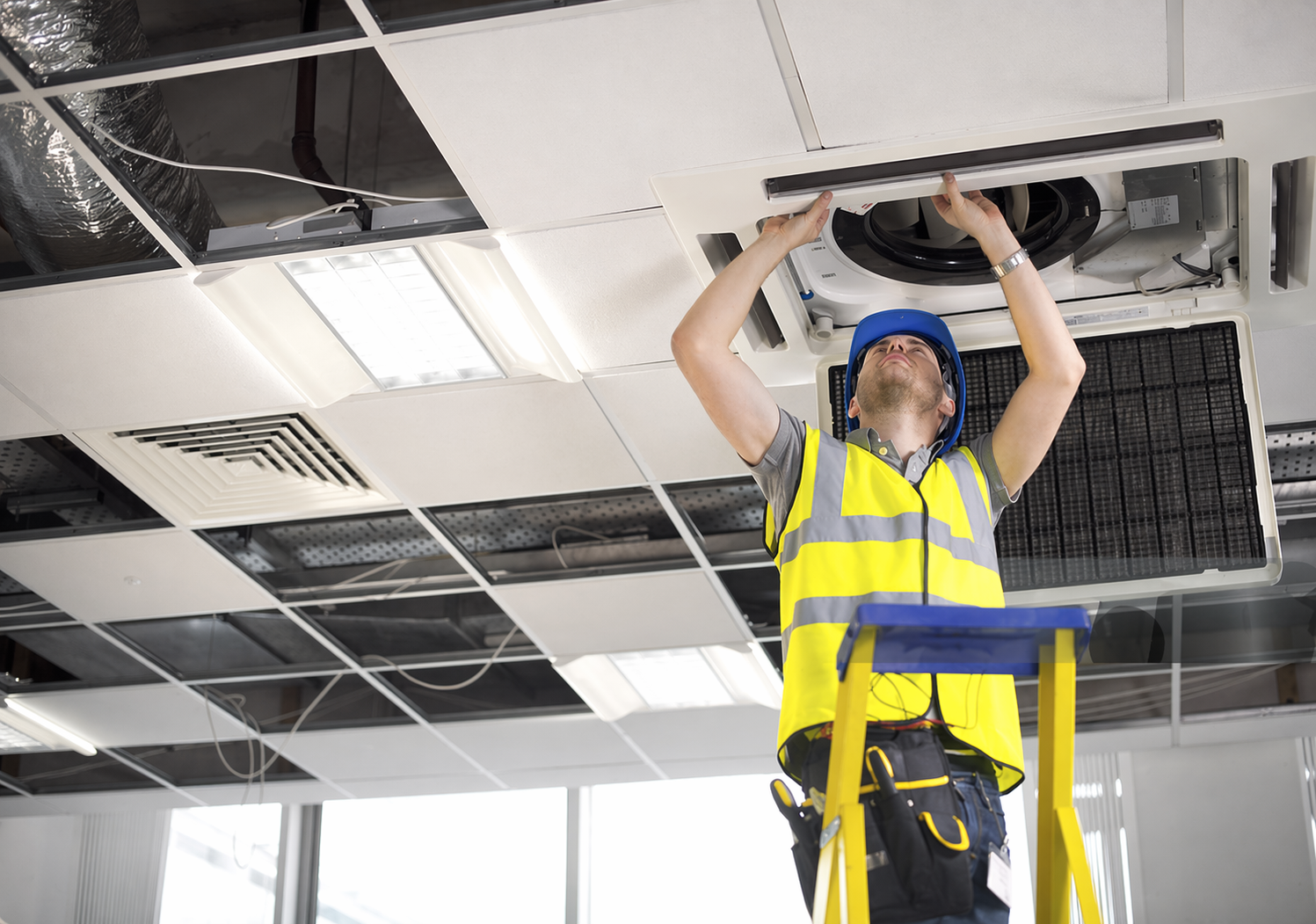 Technician servicing a ceiling-mounted HVAC unit and ductwork
