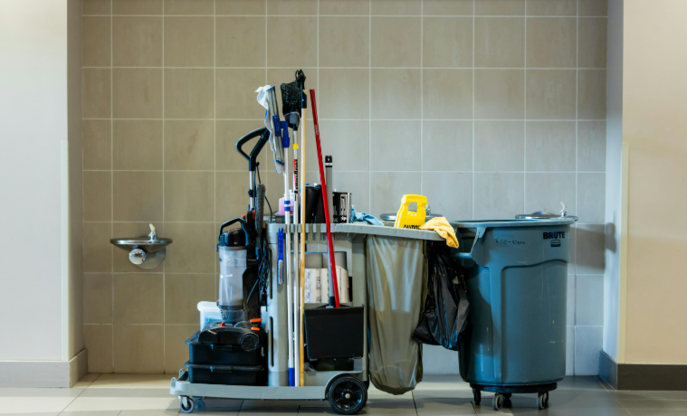 Fully stocked janitorial cart with mops, brooms, vacuum, cleaners, and waste bin